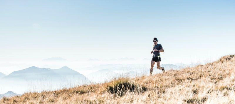 A man running on a mountain top, surrounded by a panoramic view of rugged peaks and clear blue sky.