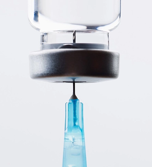 A syringe filled with liquid, positioned upright against a neutral background.