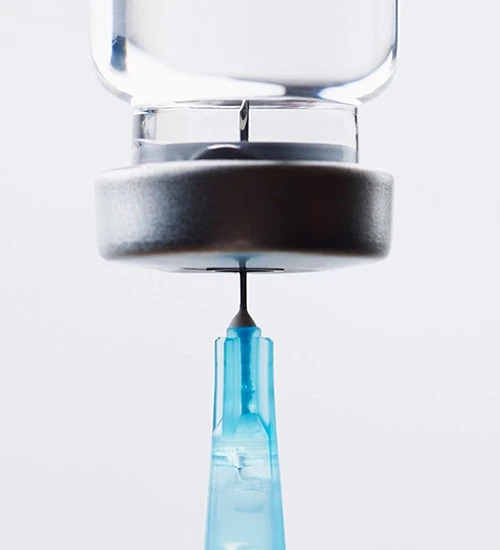 A syringe filled with liquid, positioned upright against a neutral background.