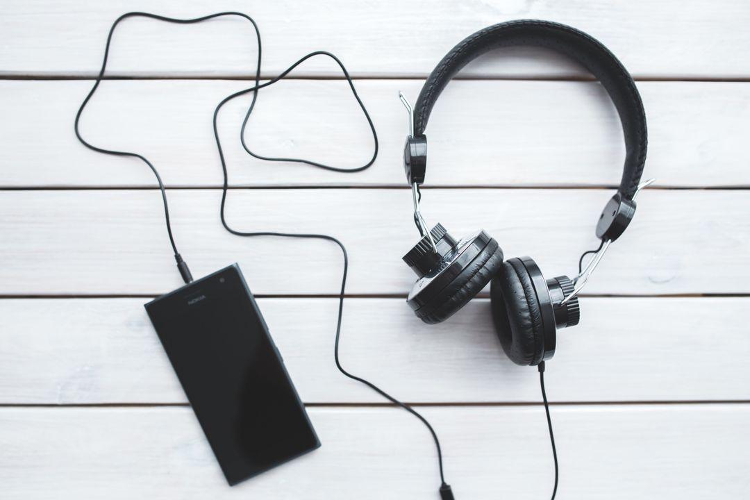 A pair of headphones and a smartphone resting on a wooden background, highlighting a casual tech arrangement.