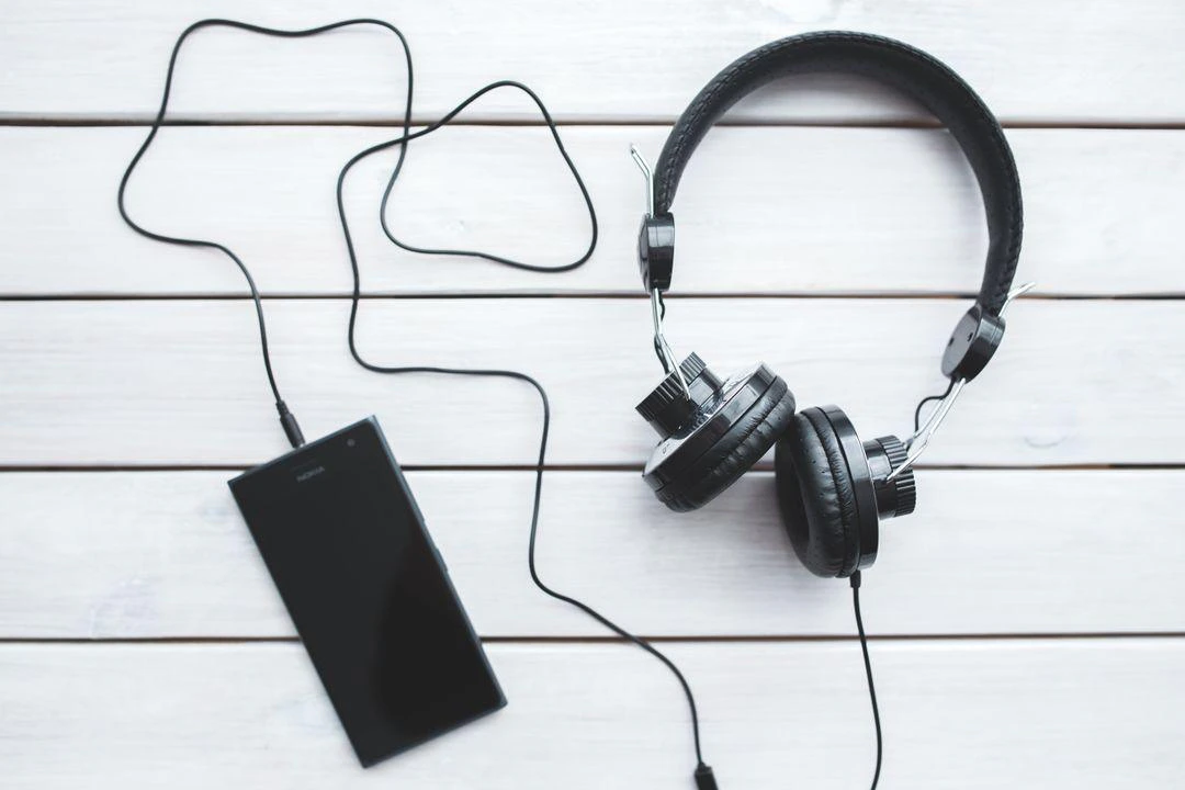 A pair of headphones and a smartphone resting on a wooden background, highlighting a casual tech arrangement.