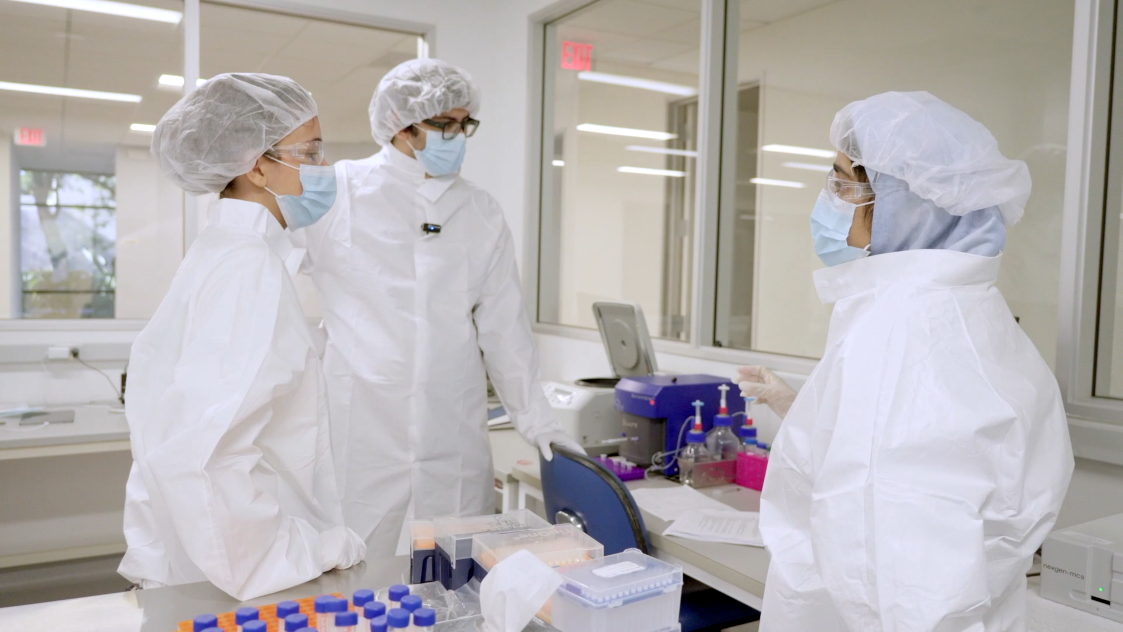 3 scientists in protective gear collaborating in a laboratory setting. 