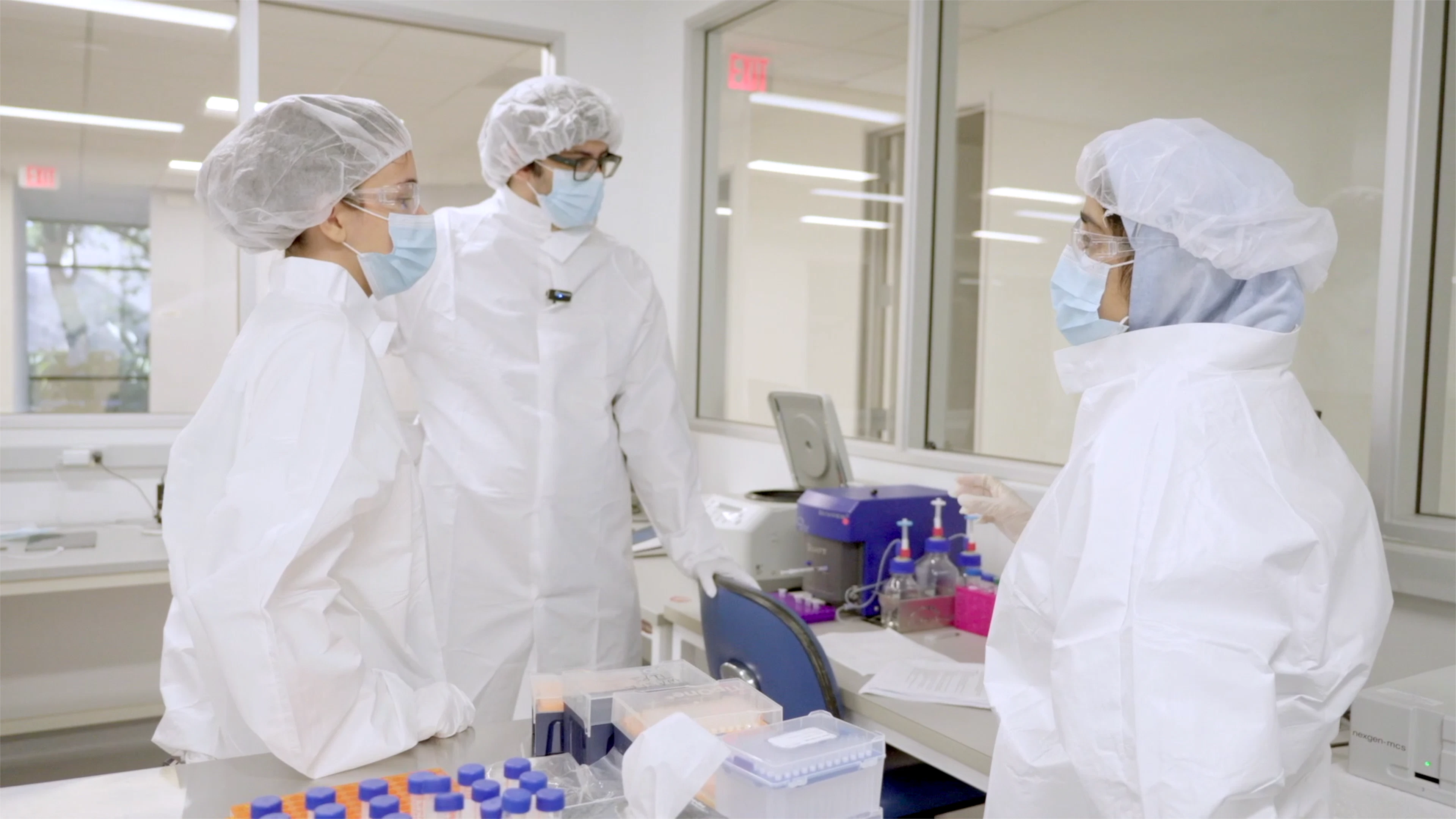 3 scientists in protective gear collaborating in a laboratory setting.