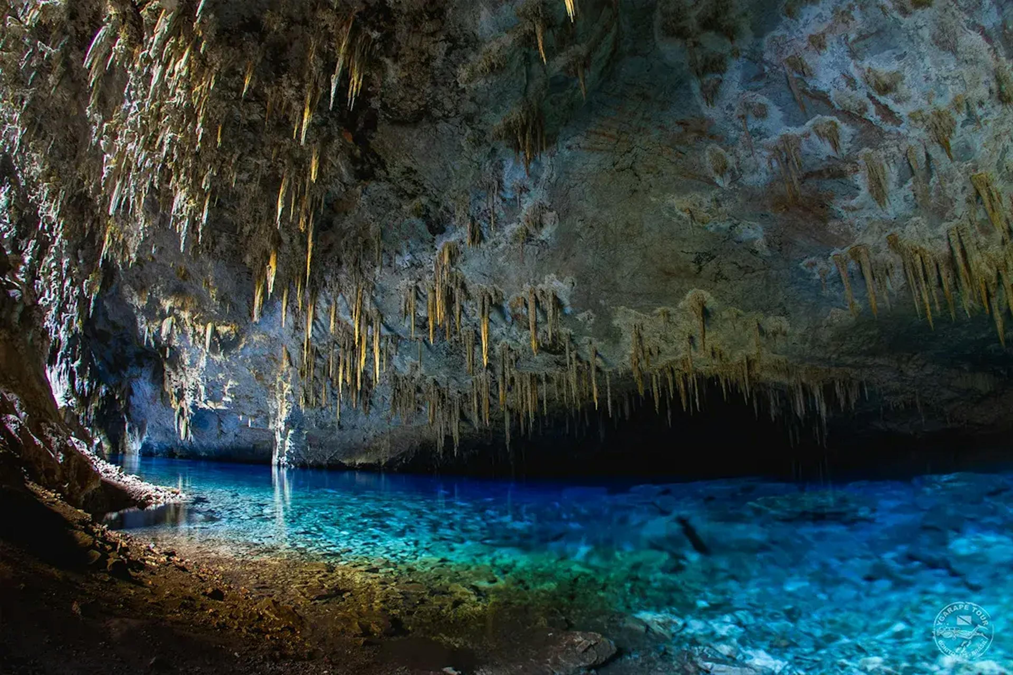 Formações rochosas pendendo do teto da gruta como gotas em direção ao lago azul