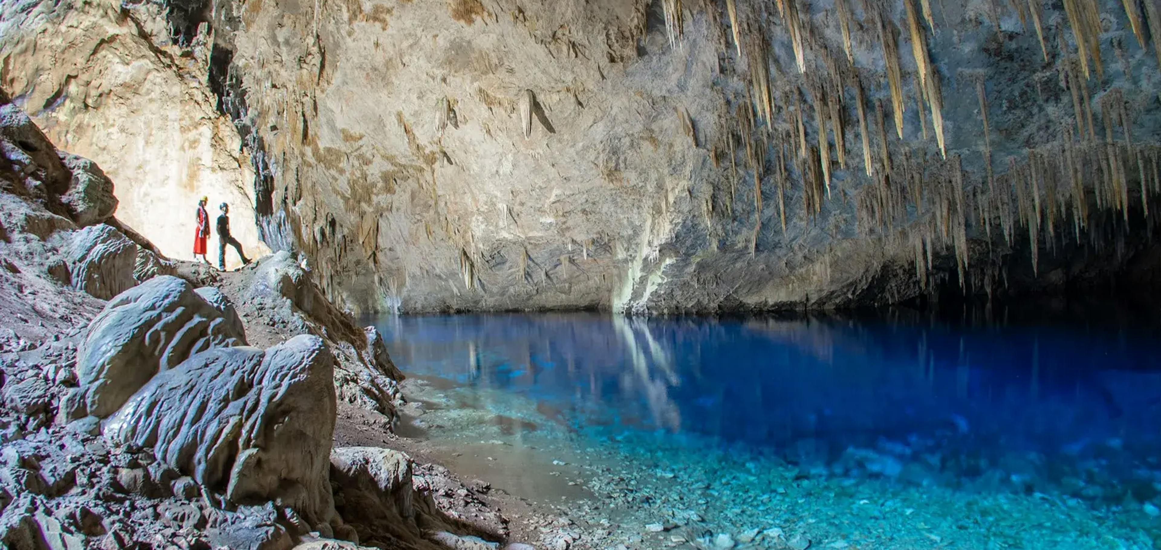 Guia turístico apresentando o interior da gruta para turista de frente para o lago de águas azuis e cristalinas