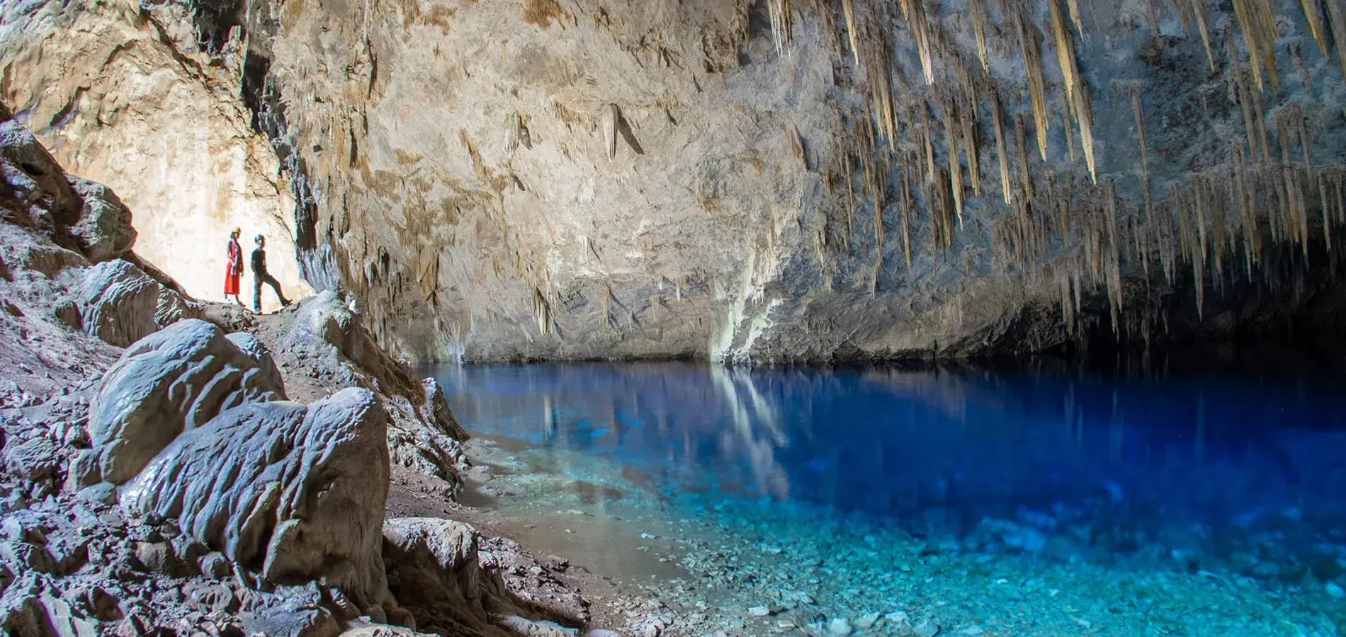 Guia turístico apresentando o interior da gruta para turista de frente para o lago de águas azuis e cristalinas