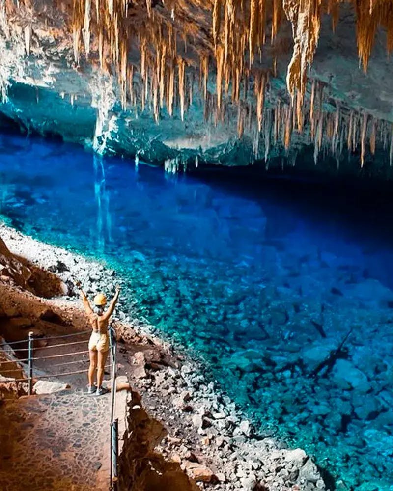 Turista de braços para cima manifestando contemplação ao avistar efeito azul exclusivo da Gruta do Lago Azul
