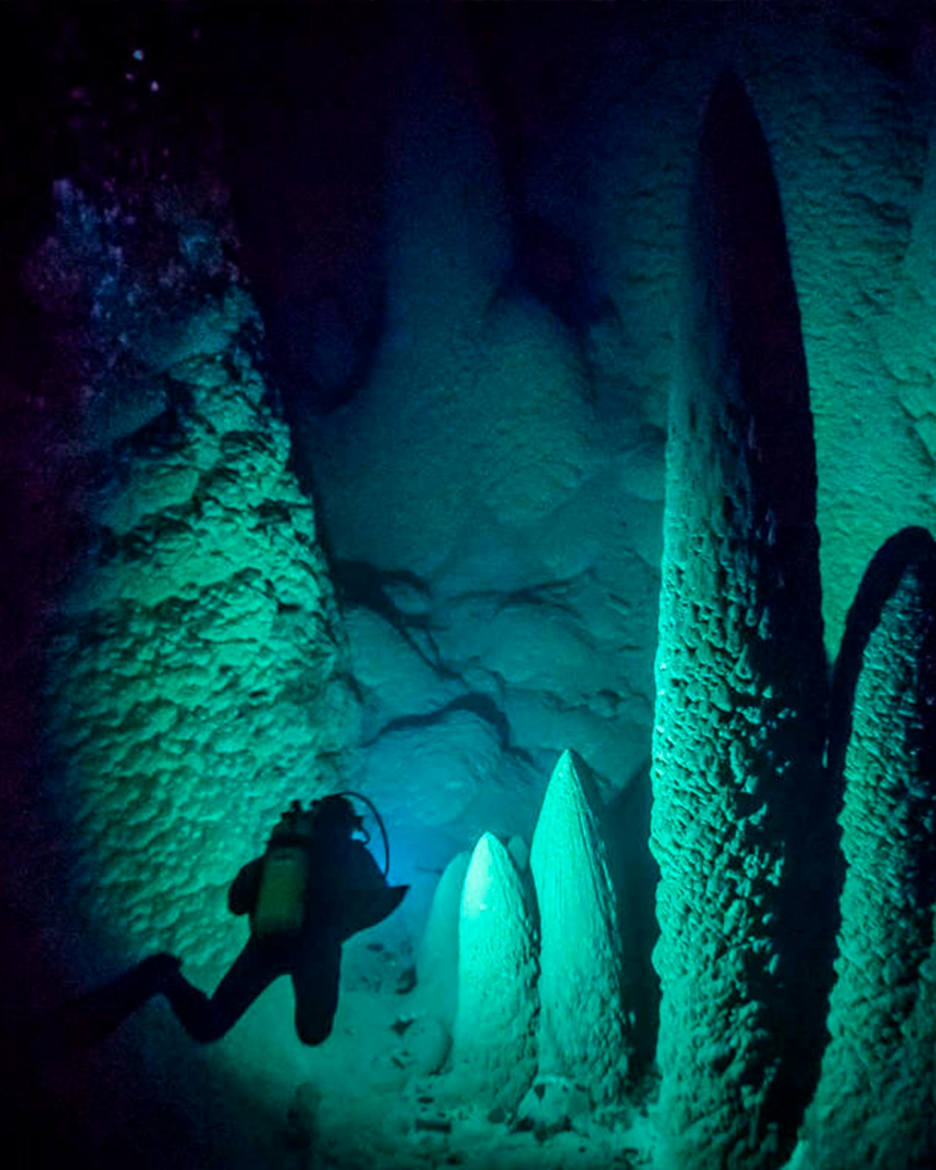 Imagem de formações rochosas em forma de cones e feitas de calcários imergindo da caverna que forma o Abismo Anhumas