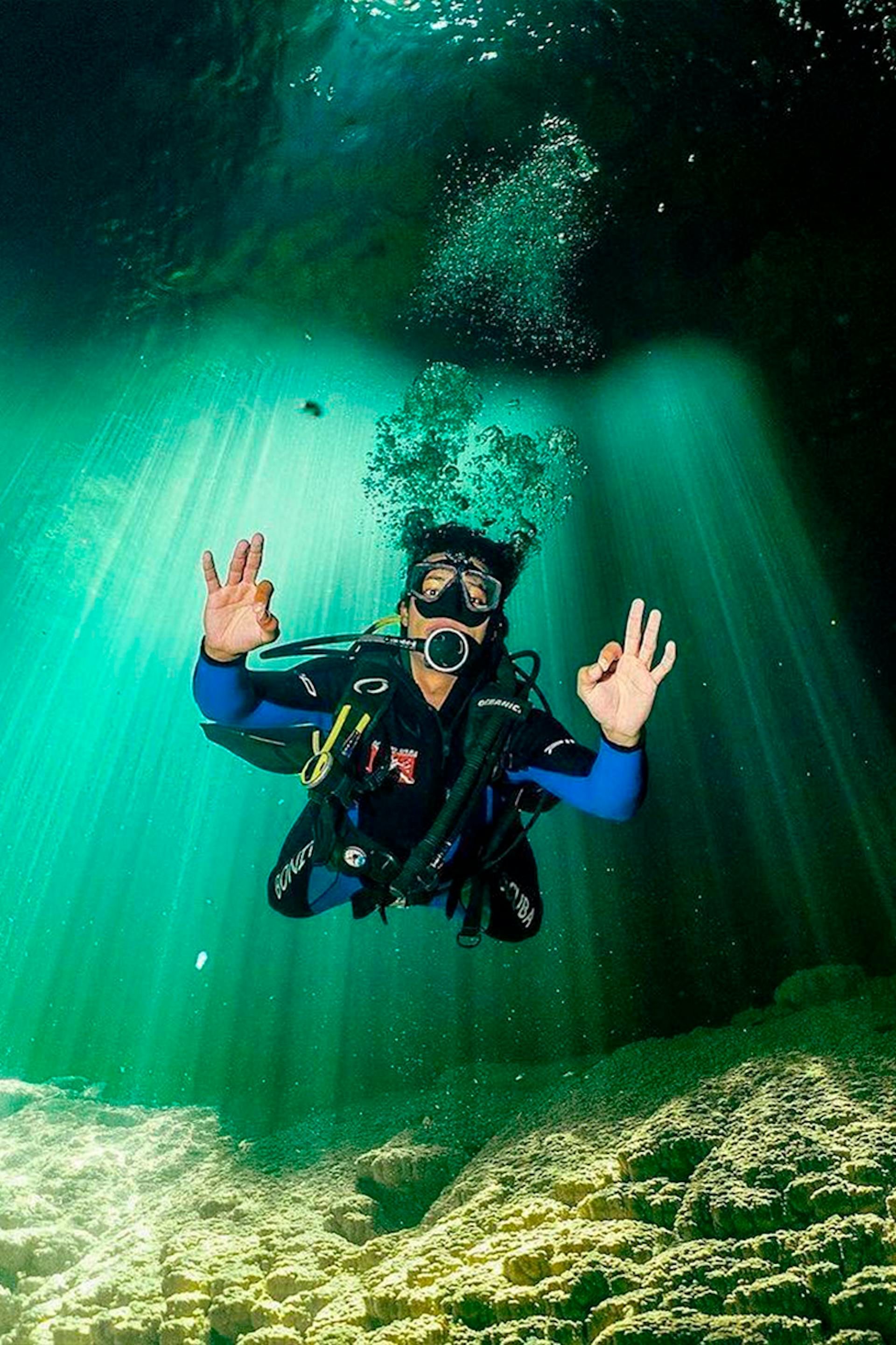 Turista submersa em mergulho no lago do interior do Abismo Anhumas com visibilidade total, acenando positivamente, ilustrando a cristalinidade da água