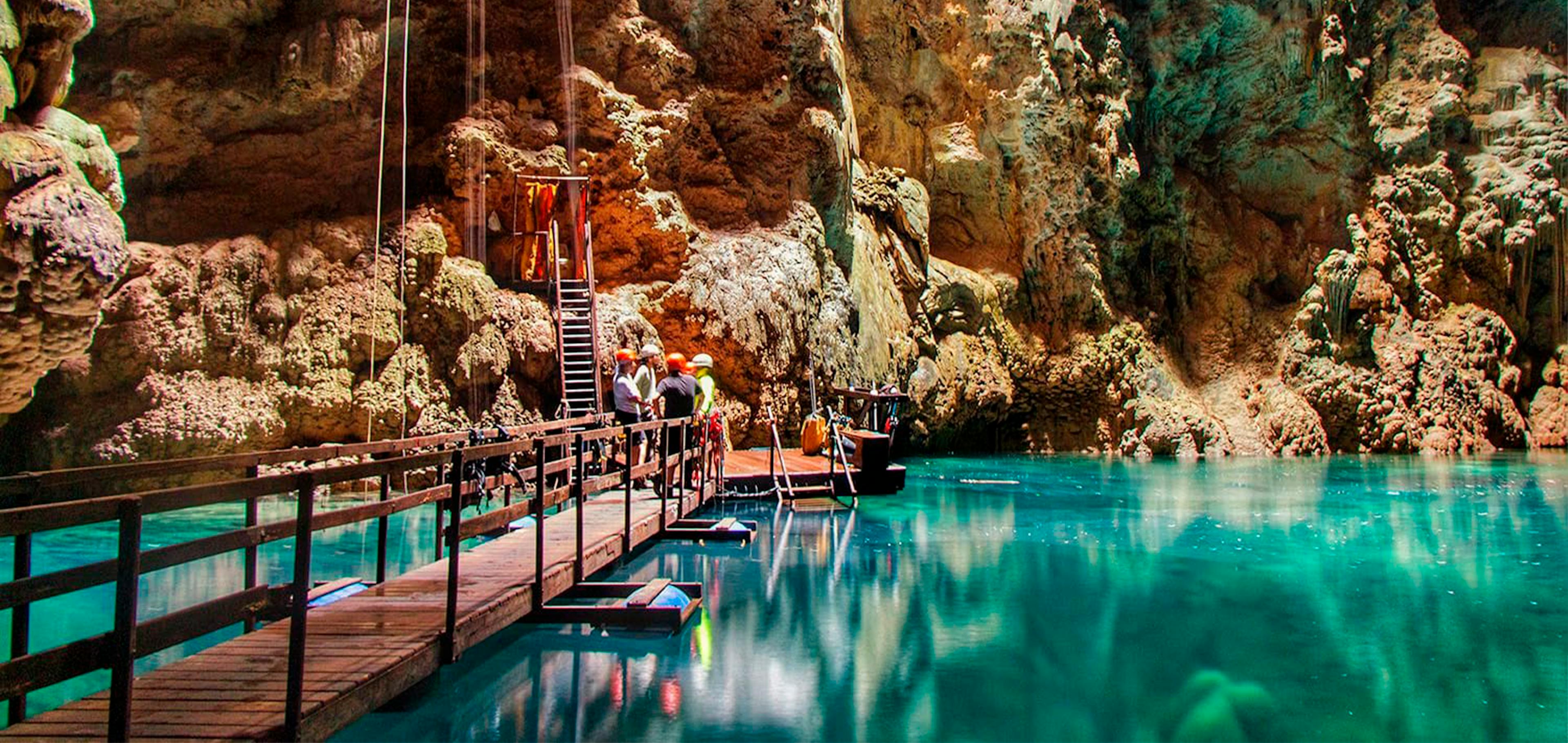 Grupo de turistas no interior do Abismo Anhumas contemplando formações de rochas e lago cristalino do interior da caverna