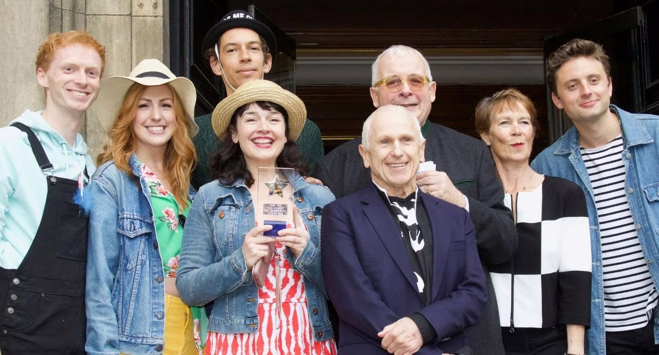 An image of people standing in front of the door of a church. All of them are smiling and posing with an award.