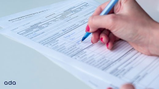 A person holding a pen in her hand and filling out an anmeldung form.