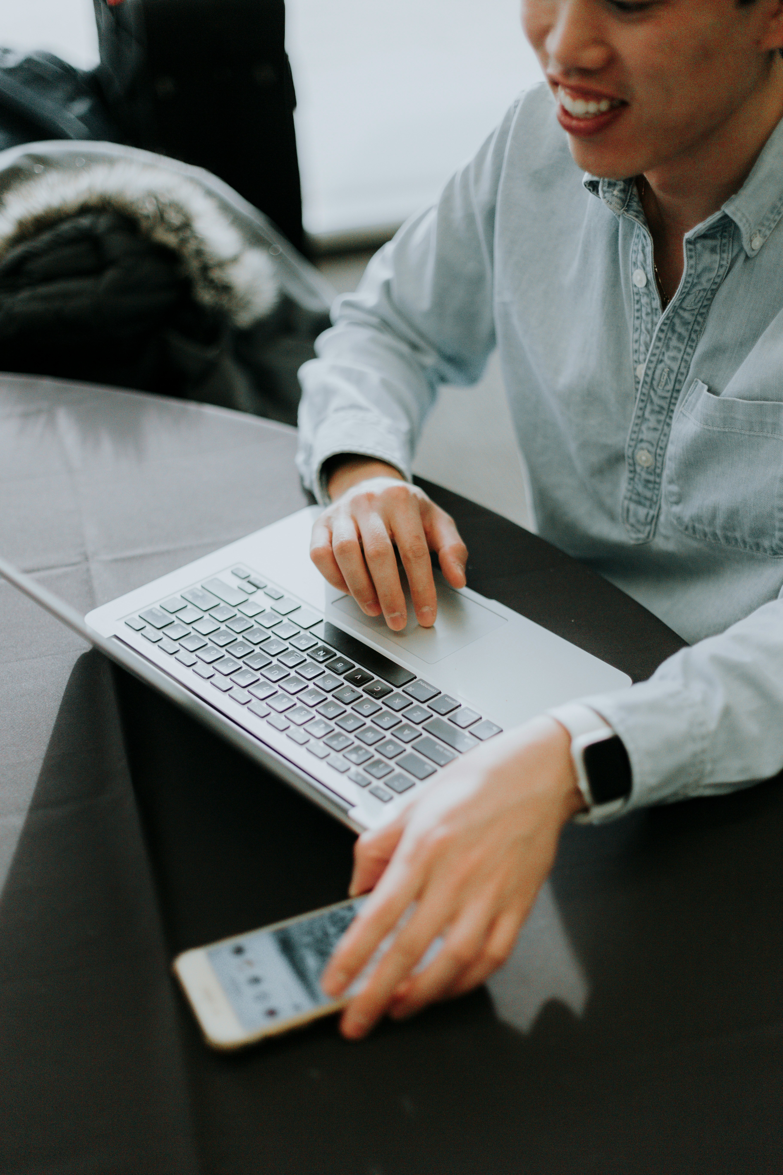 Business professional in his mid-30s sitting on a bench with a laptop and smartphone, symbolizing modern communication, accessibility, and customer contact in the electronics industry.