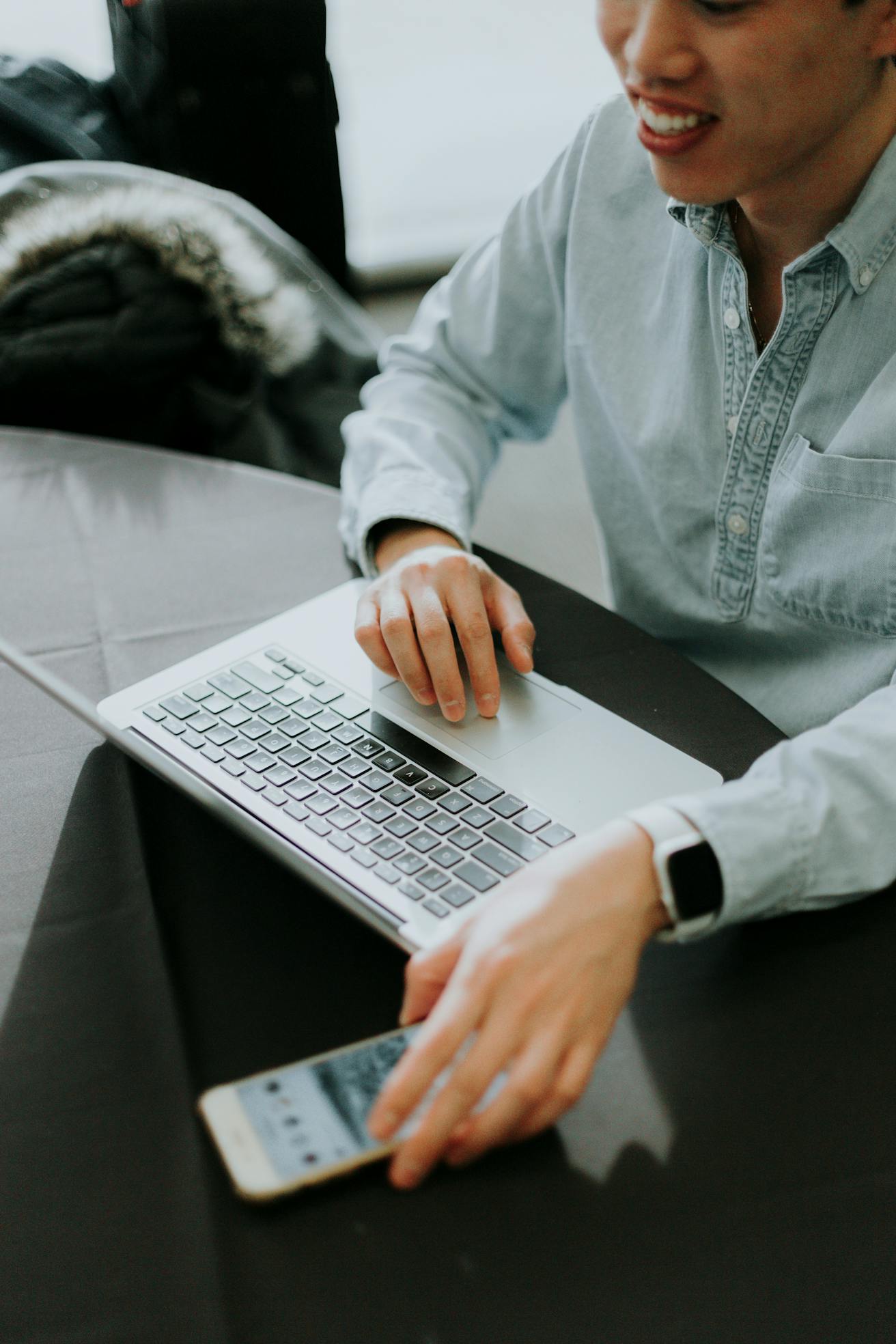 Business professional in his mid-30s sitting on a bench with a laptop and smartphone, symbolizing modern communication, accessibility, and customer contact in the electronics industry.