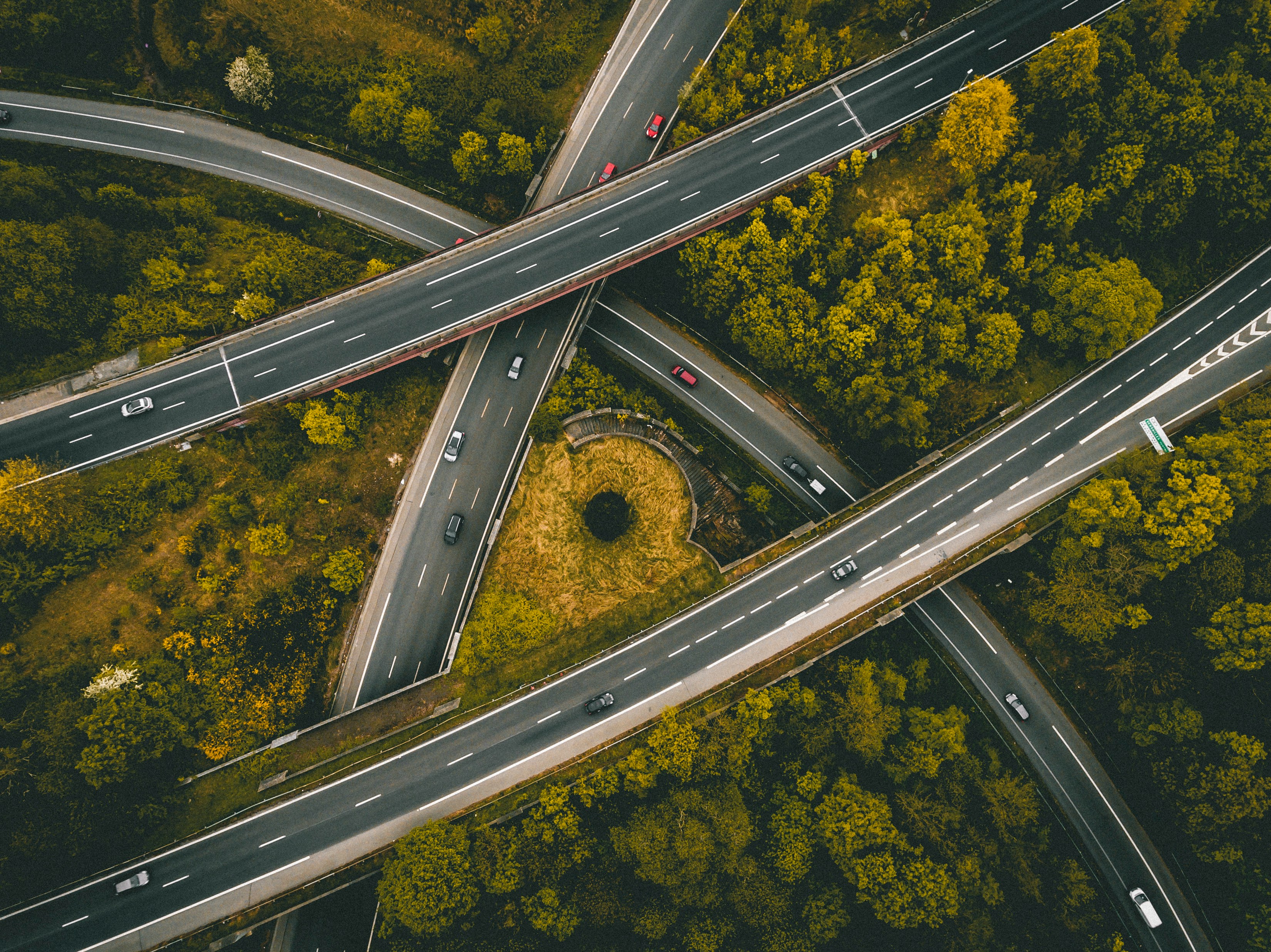 Aerial view of intersecting roads surrounded by forest landscape, symbolizing complex logistics networks and infrastructure in global distribution.