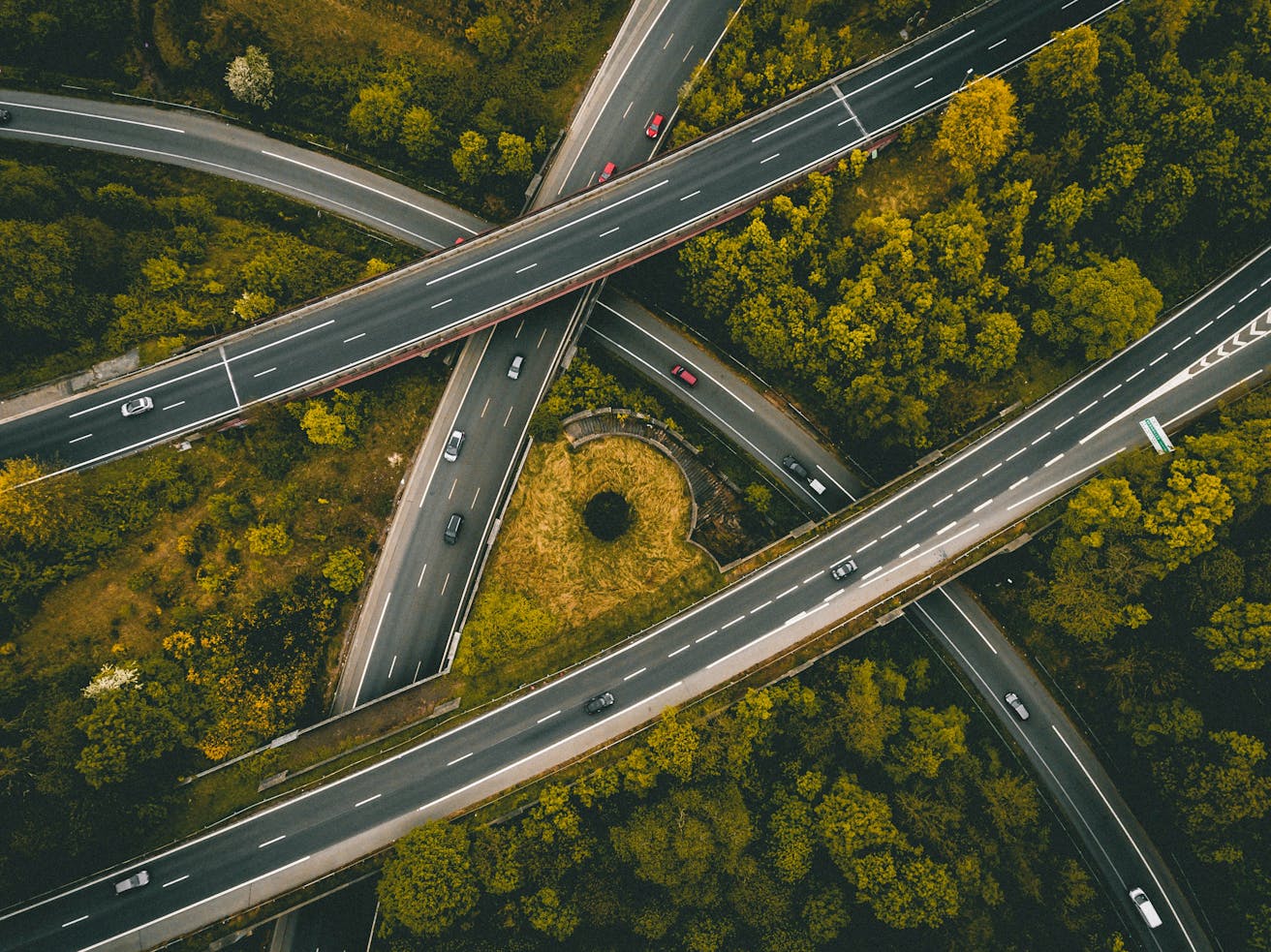 Aerial view of intersecting roads surrounded by forest landscape, symbolizing complex logistics networks and infrastructure in global distribution.