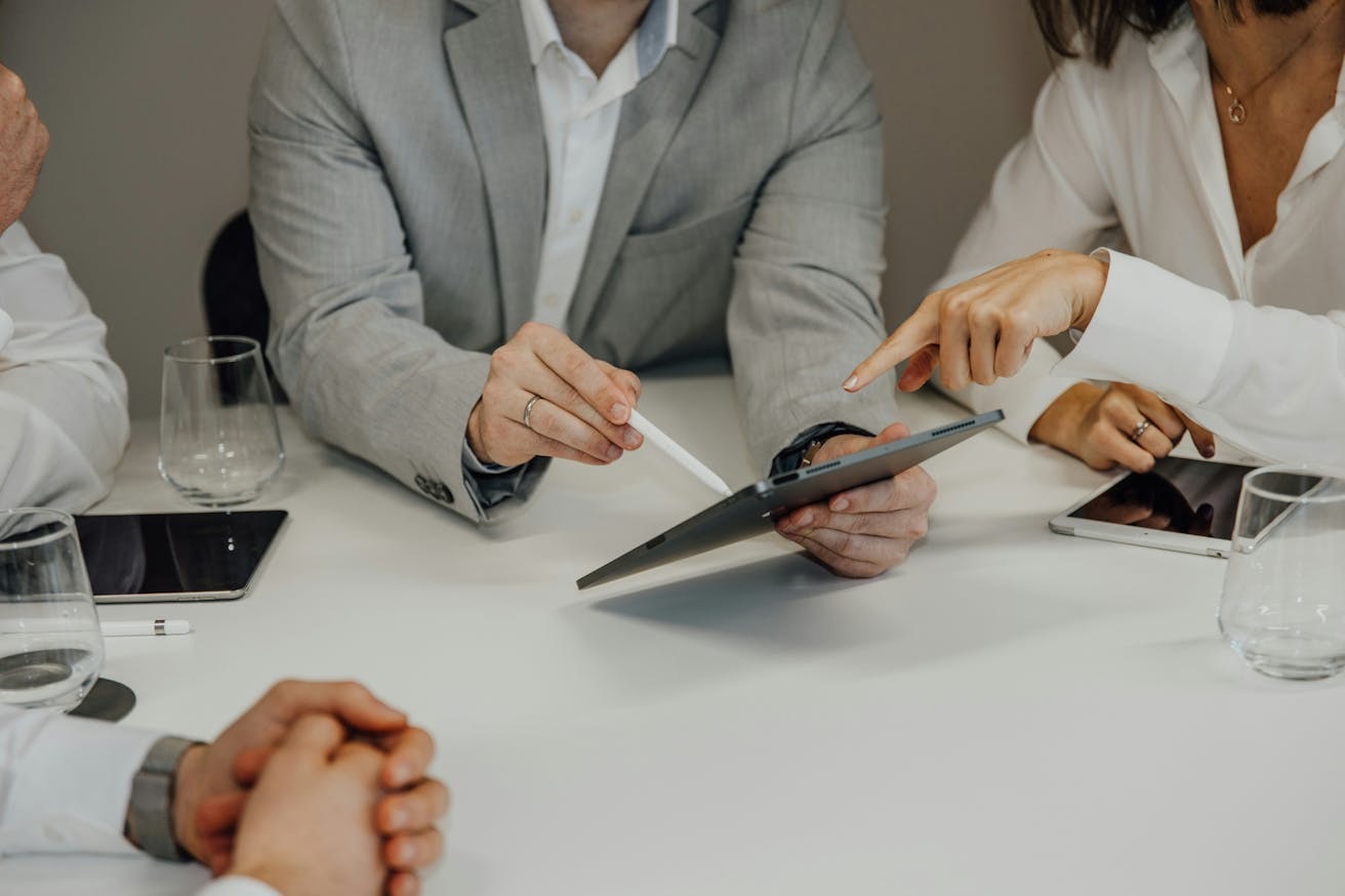 Close-up of three business professionals in suits having a meeting at a table, with focus on their hands – symbolizing collaboration, decision-making, and corporate strategy.