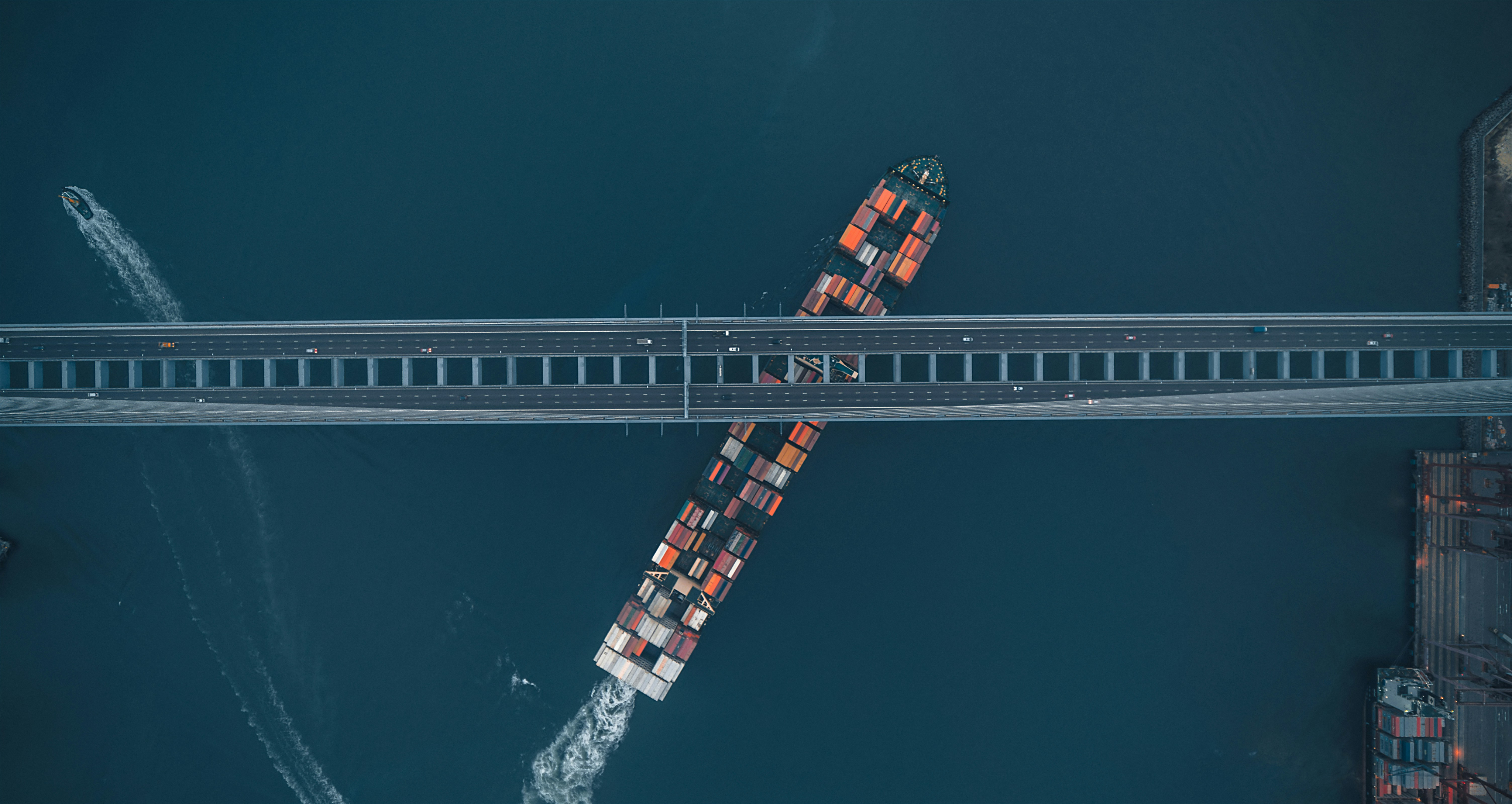 Container ship passing beneath a busy highway bridge, symbolizing global logistics and wholesale distribution of electronic components