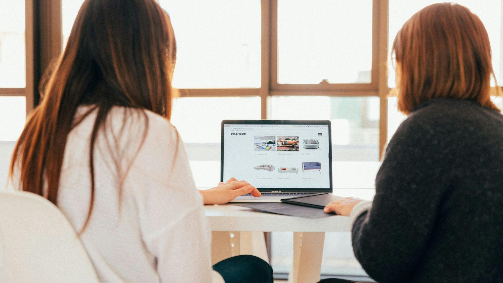 two women sitting at a desk looking at a website