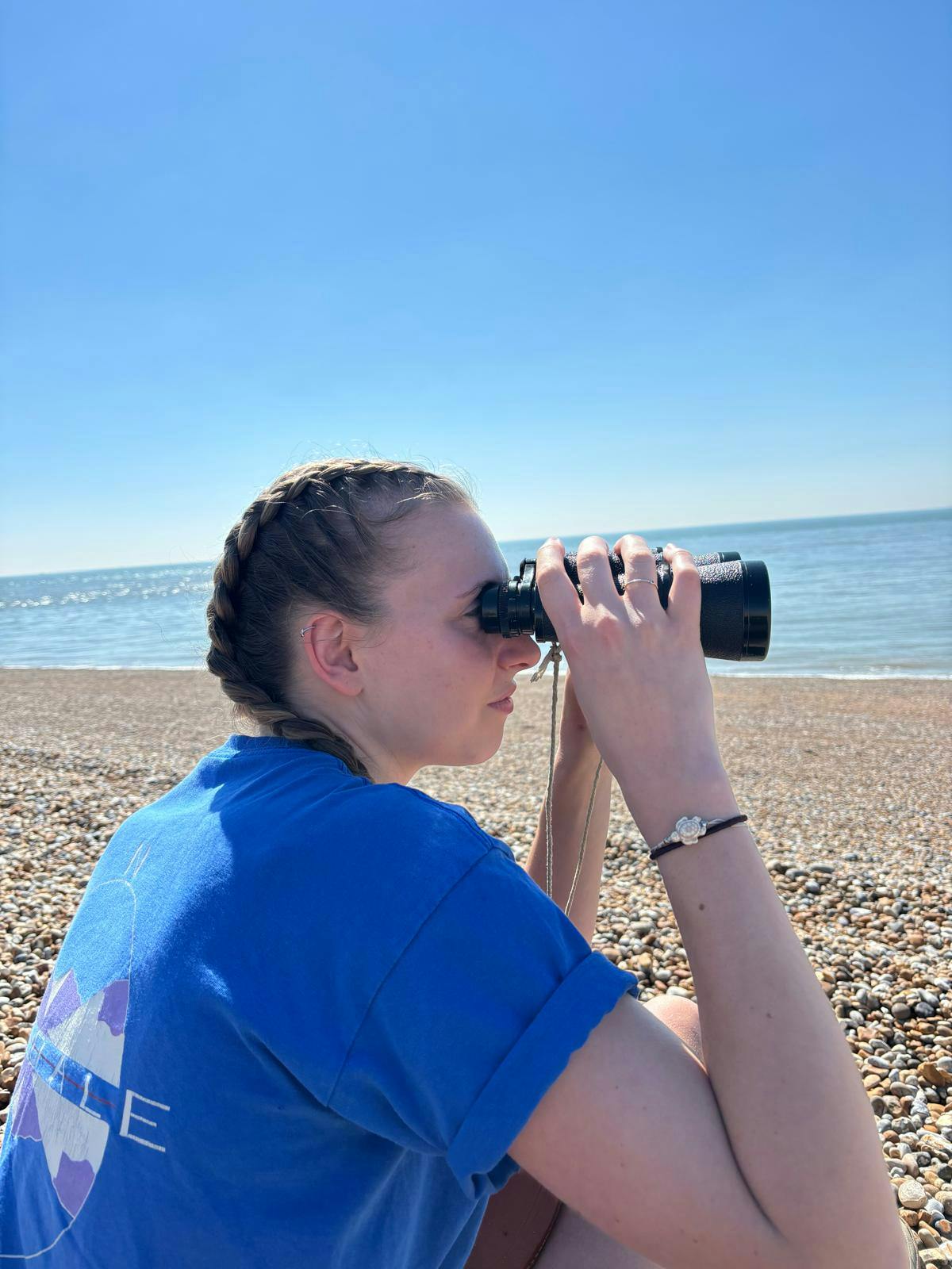 Emmie sat on a beach looking through binoculars