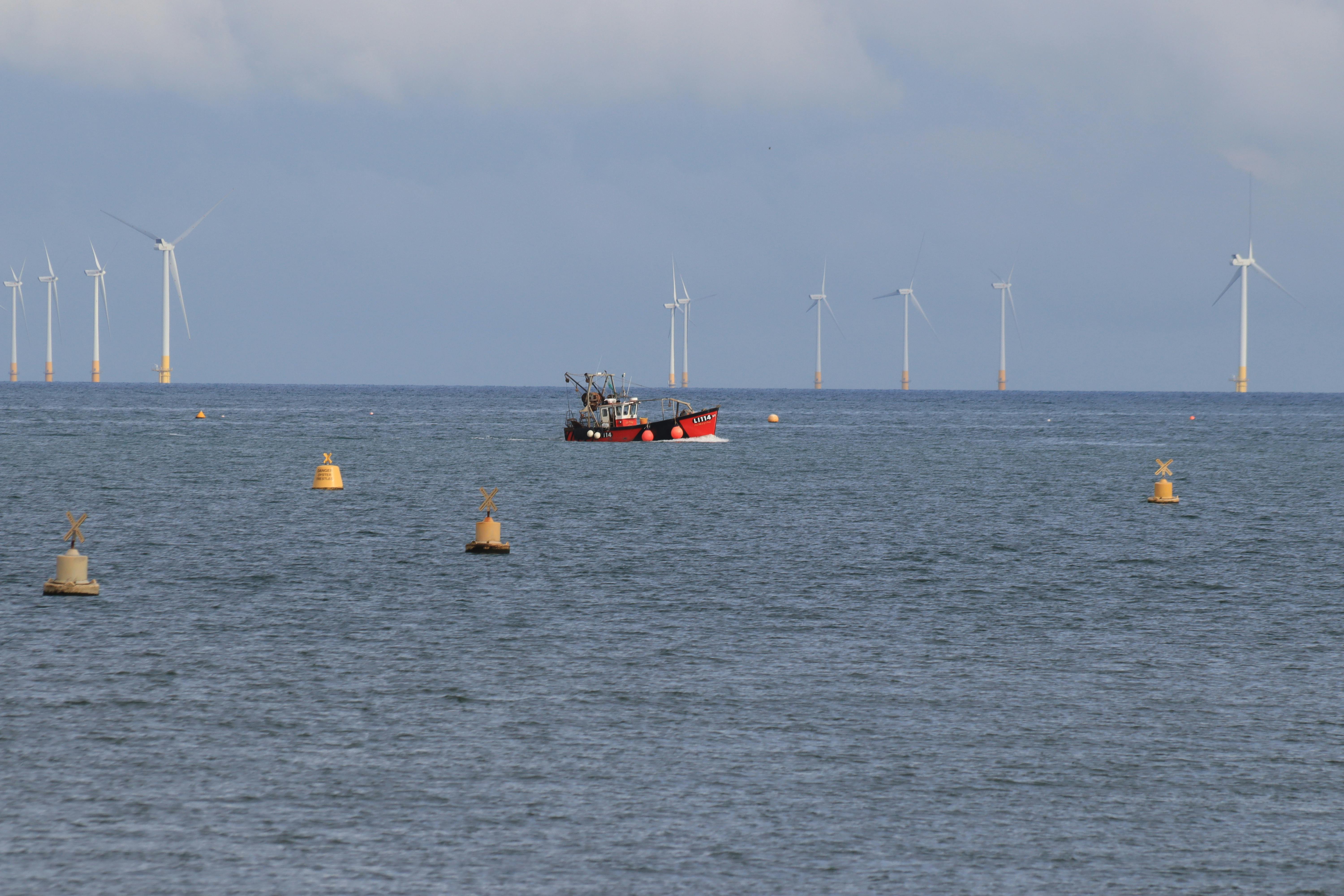 A fishing boat at sea, with 10 off-shore wind turbines visible on the horizon