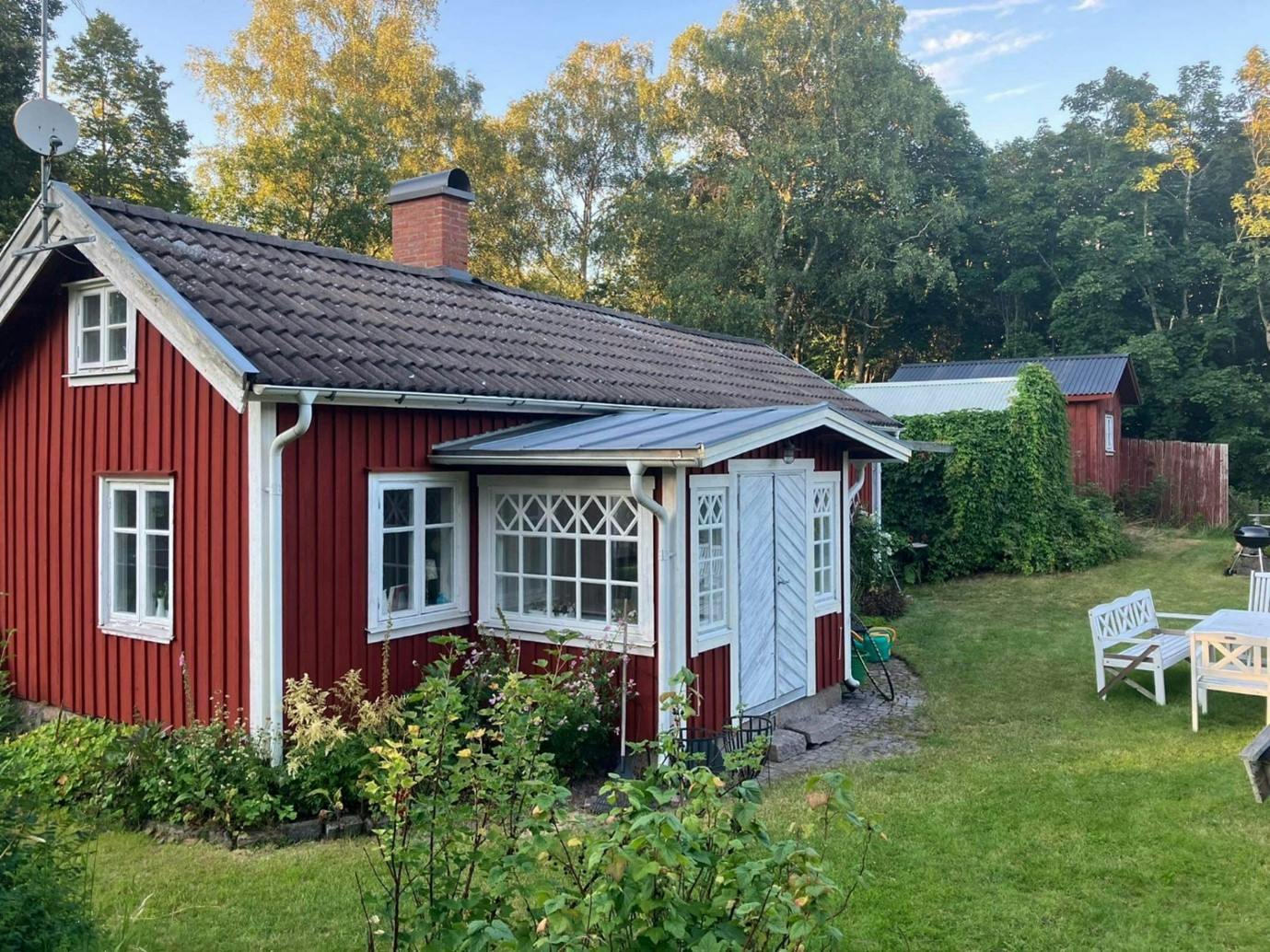 Linn's home, a red cottage with white doors and windows, surrounded by greenery