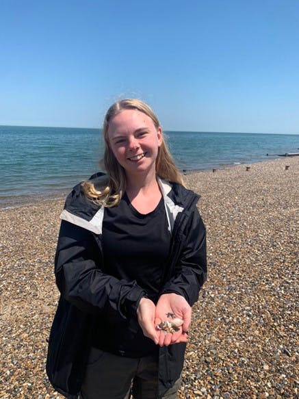 Linn on a stony beach holding a selection of shells