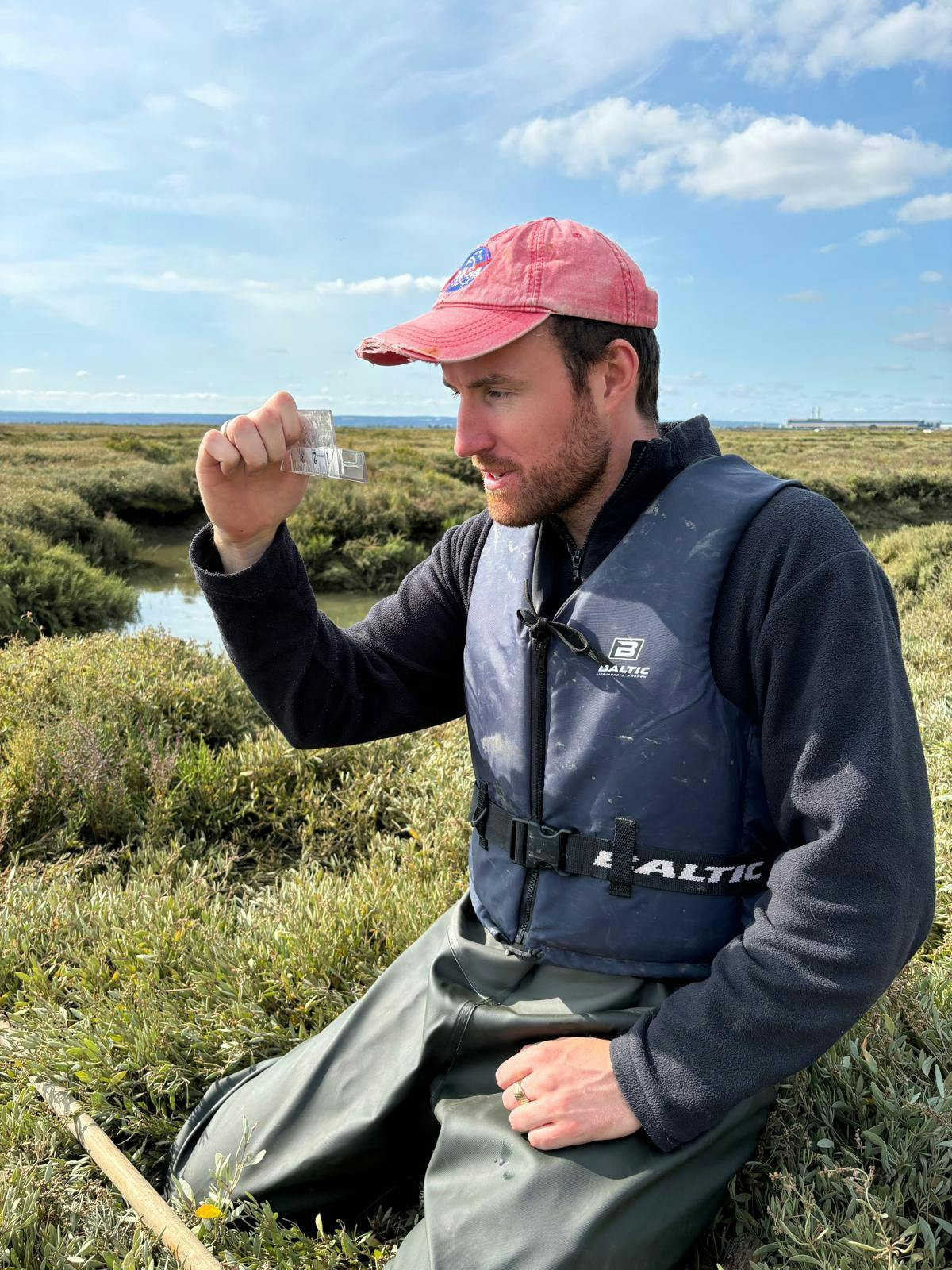 man looking at a fish on a scale knelt down on saltmarsh