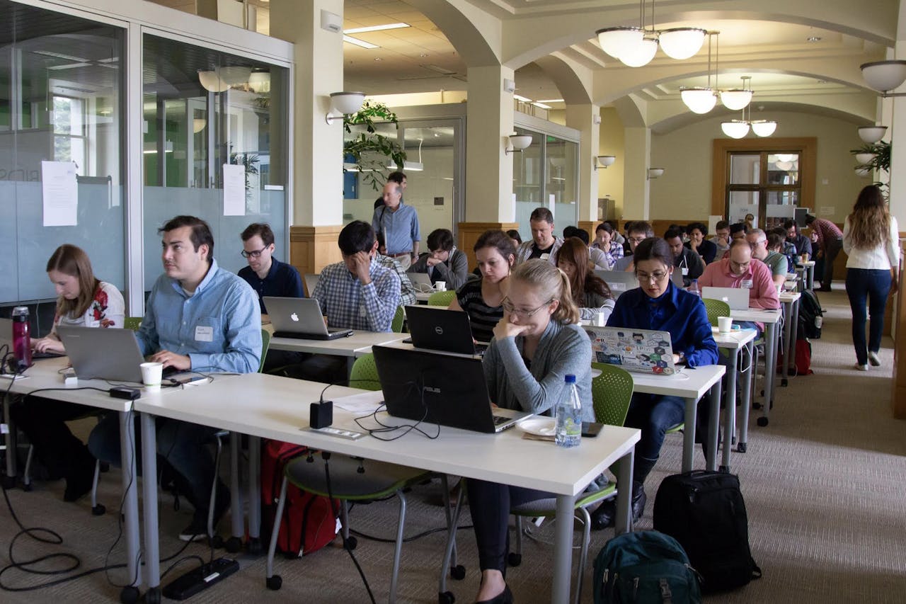 A room of tables with people work on laptops - apparently a hands-on workshop setting