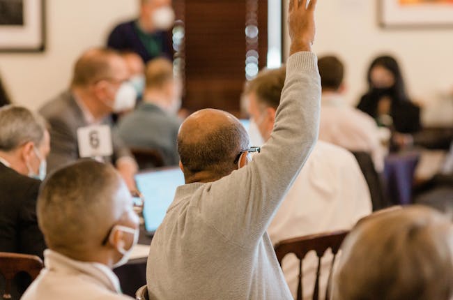 a person raising their hand to be called on in a room full of people at tables