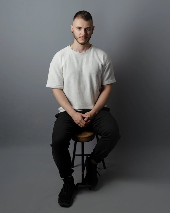 A portrait of Adrian Wilhelm on a chair in a studio.