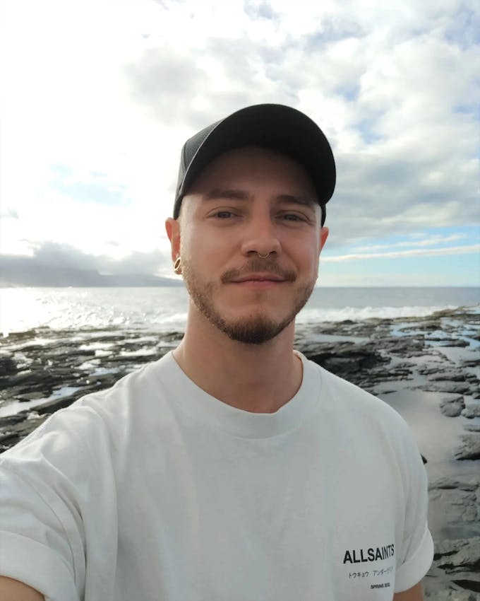 A portrait of Adrian Wilhelm on a rocky beach with ocean view.