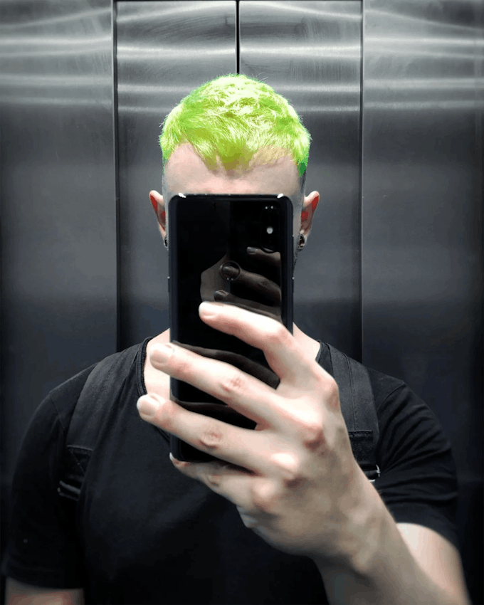 A mirror selfie of Adrian Wilhelm with neon green hair in an elevator.