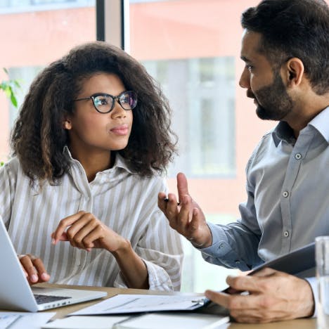 Two people at a desk looking at documents and talking