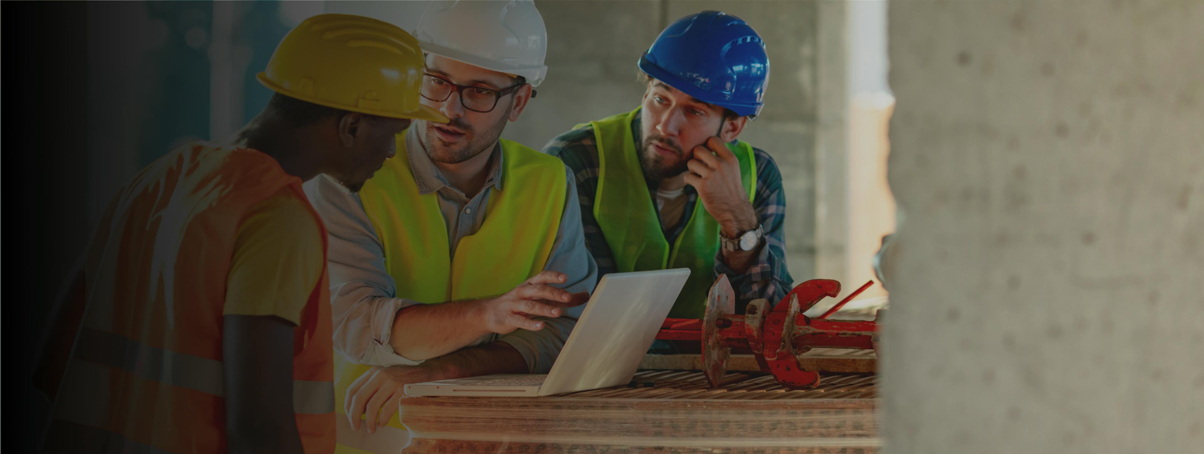 Three people on a building site gathered around a computer and having a discussion