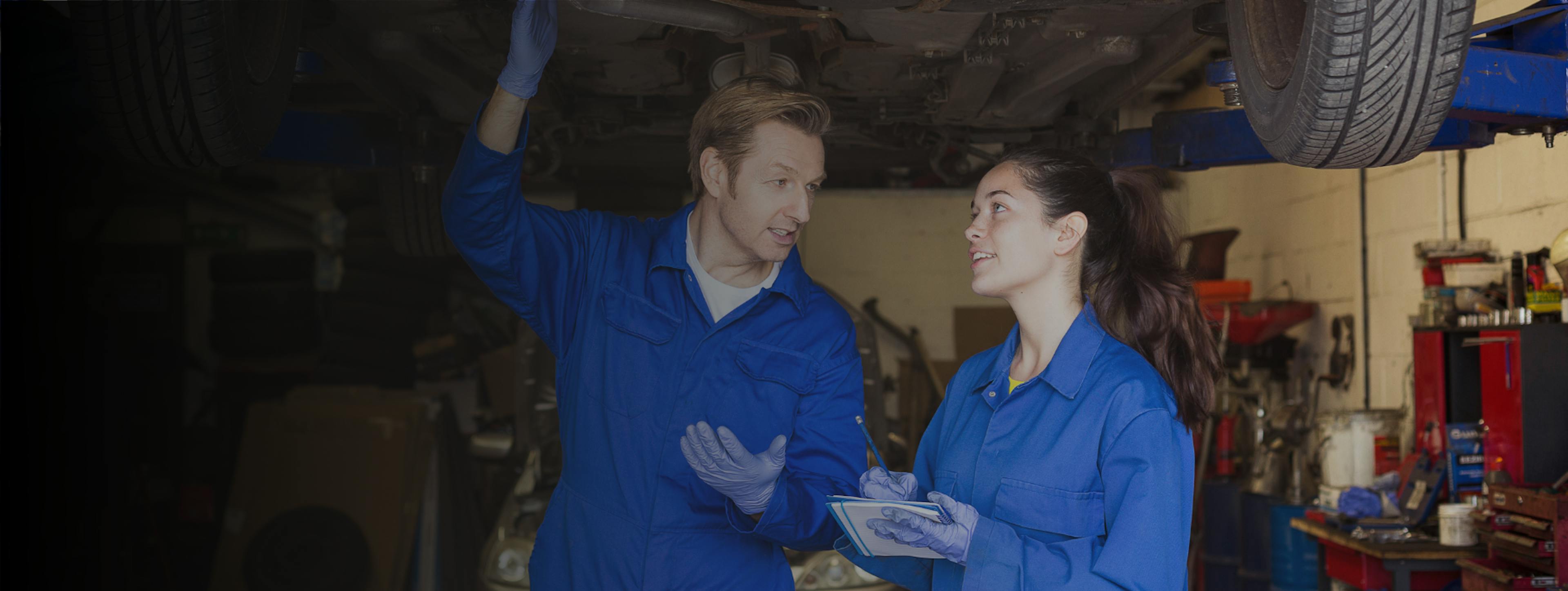A male and female mechanic looking at the underside of a car