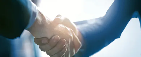 Bild eines "Händeschüttelns", man sieht zwei Unterarme in Anzug und die verschränkten Männerhände