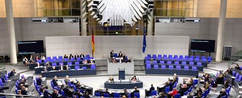 Blick in den Bundestag während einer Besprechung, es nehmen einige Personen teil, im Hintergrund der Bundesadler