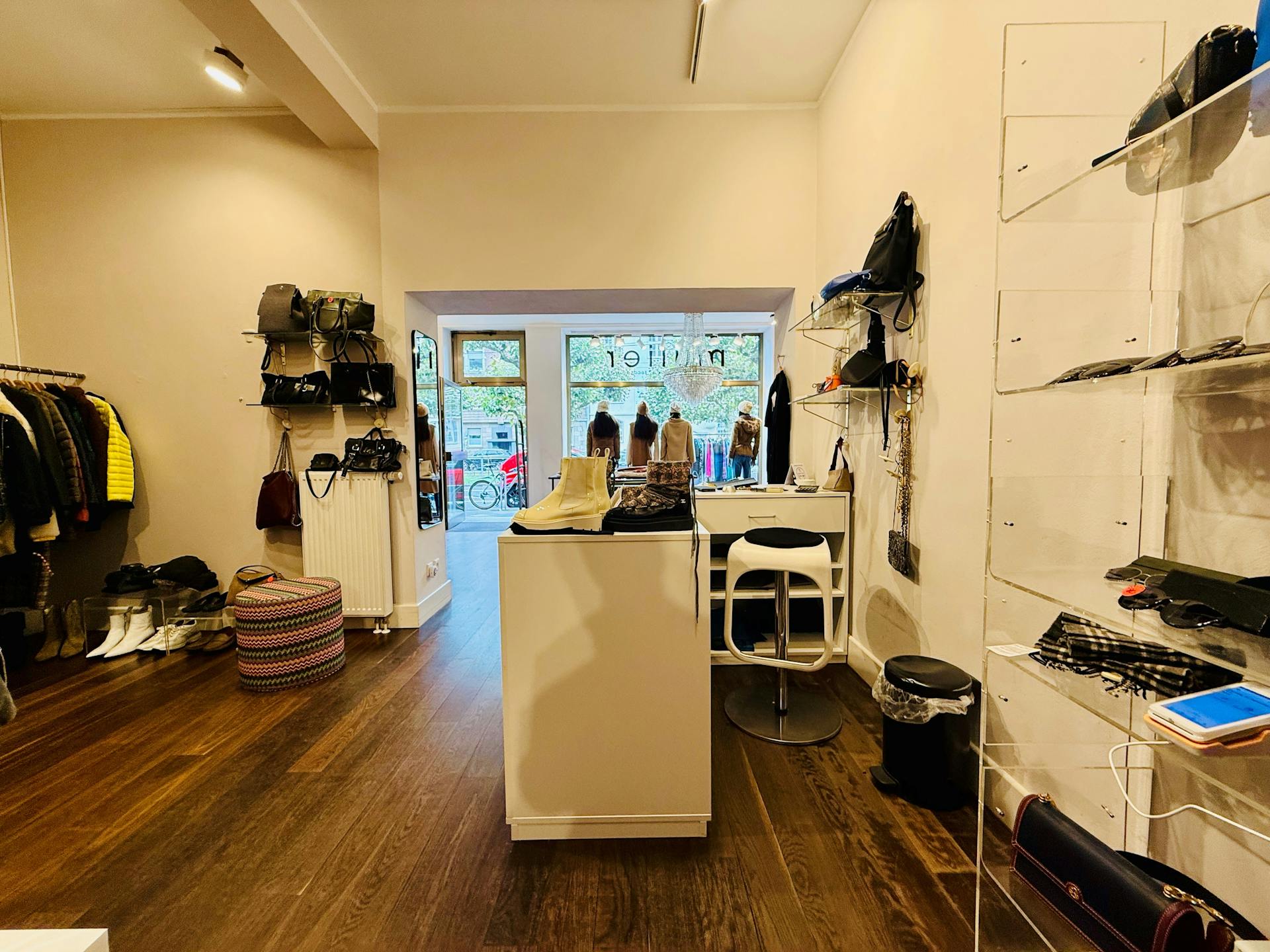 Blick aus einem Ladenlokal durch das Schaufenster nach draußen. In dem Laden hängen recht und links Textilien und wir mit einem warmen Licht beleuchtet. Der laden hat eine dunklen Holzboden.