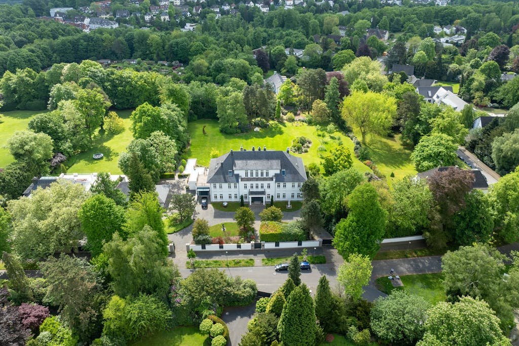 Weiße Villa mit viel Garten und Bäumen drumherum