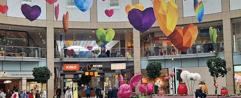 Einblick in ein buntes Shoppingcenter mit vielen Schaufenster und Menschen in Bewegung.