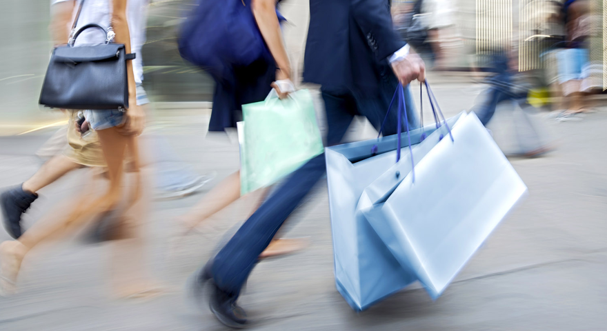 Bild von Personen, Ausschnitt ab Schulter, welche Taschen und Einkaufstaschen tragen und durch eine Fußgängerzone gehen