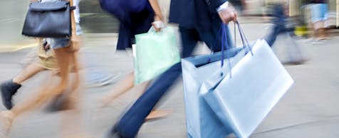 Bild von Personen, Ausschnitt ab Schulter, welche Taschen und Einkaufstaschen tragen und durch eine Fußgängerzone gehen