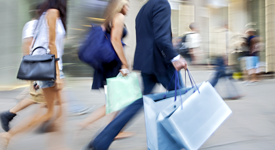 Unscharf dargestellte Menschen, die mit Einkaufstüten in den Händen vorbeigehen. 
