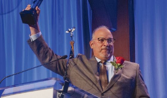 A senior engineer stands on stage and holds a BOMA award for his excellence in building management