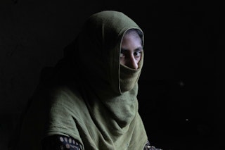 Young woman sits in a green hijab in dim light
