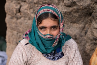 A woman in a coloured headscarf and stone wall in the background