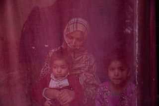 With a thin sheet obscuring them through a window, a veiled woman sits with her two young daughters -- one a toddler on her lap