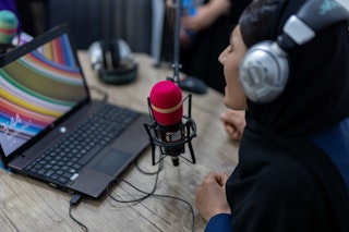 A woman wearing headphones speaks on a red radio microphone.