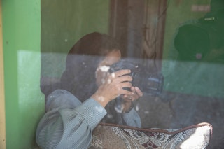 A woman with a camera takes photos through a window.